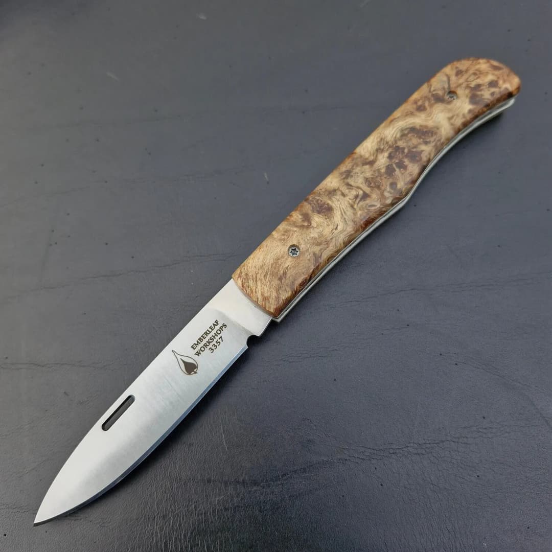 An Aquila slip joint, project 3357, open on dark leather, with a burr wood handle
