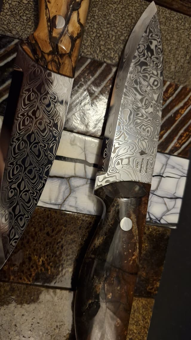Two Damascus blades over a bed of handle-material slabs