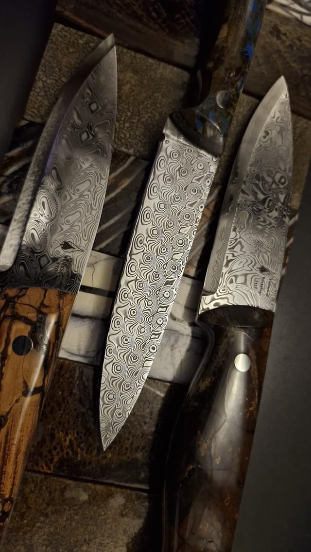 Three Damascus blades on a bed of handle-material slabs