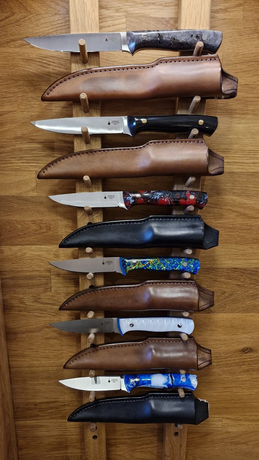 Finished Emberleaf knives drawn from their hand-made leather sheaths on a workshop display rack