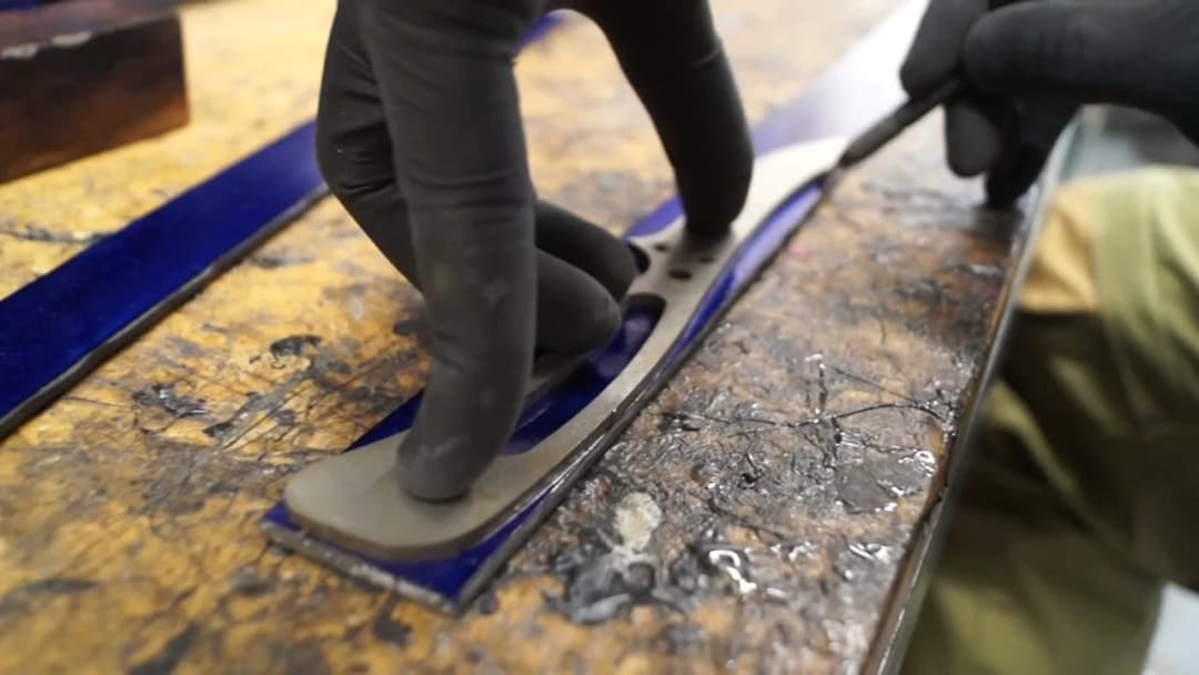 Black-gloved hands lifting a freshly cut blade blank from a Damascus billet, blue masking tape edges
