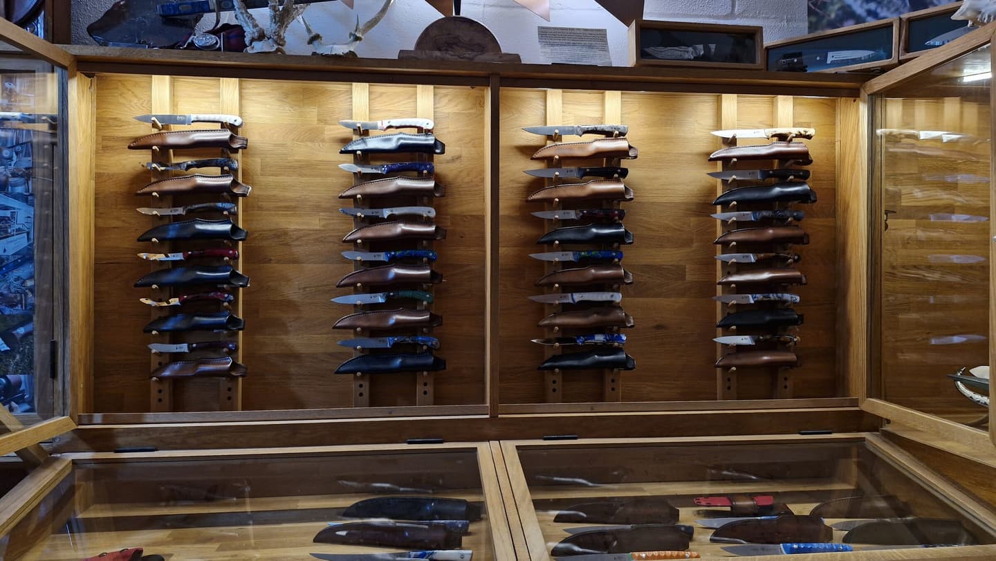 Oak display cabinets in the Emberleaf showroom, racks of finished knives in leather sheaths under warm light